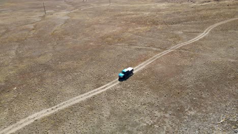 Truck-following-a-dirt-road-in-a-desert---aerial-view