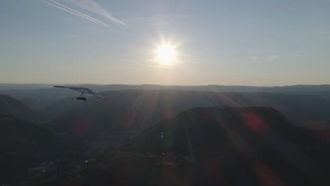 Schöne-Drohnenaufnahme-Eines-Hängegleiters,-Der-Bei-Sonnenuntergang-In-Den-Bergen-Fliegt