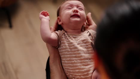 Top-close-view-of-a-brunette-man-holding-a-little-baby-girl-in-his-arms-in-a-light-brown-apartment.-Over-the-shoulder-of-a-happy-young-father-holding-his-little-baby-daughter-in-his-arms