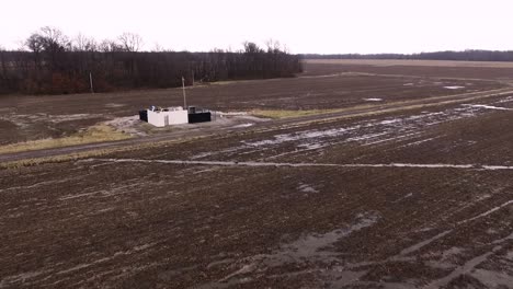 Aerial-flyover-of-a-pump-jack-operating-in-an-open-field-with-water-and-snow-in-it