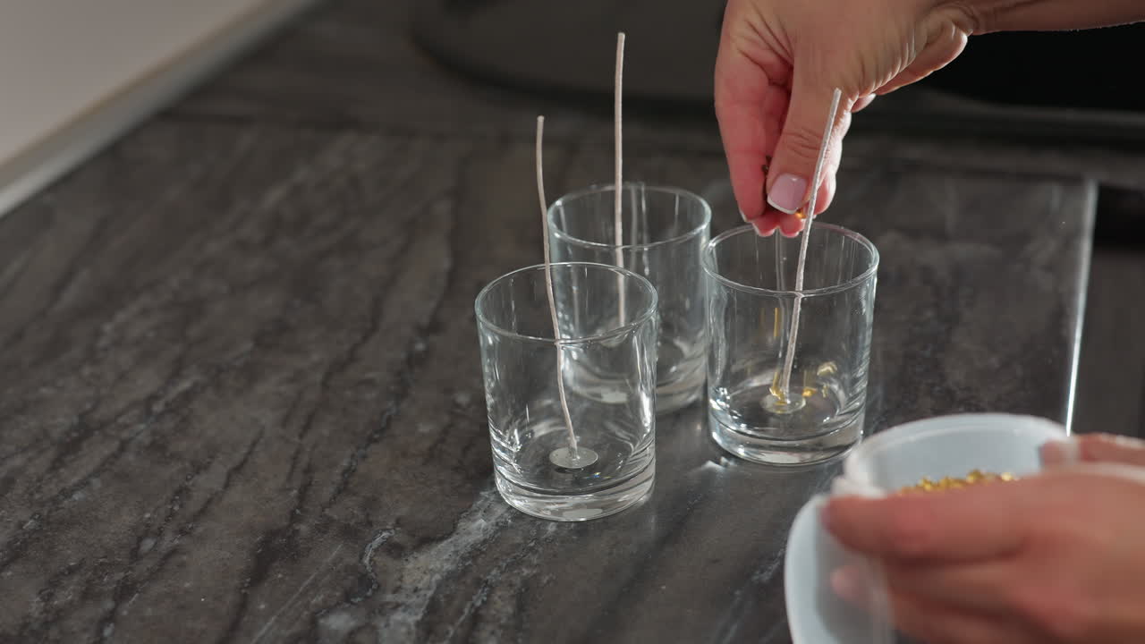 hand view of designer carefully pouring brown beads into glass cup, preparation for creative project, artistic process in progress, beads arrangement, organized workspace on kitchen countertop