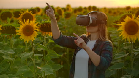 Die-Studentin-Mit-Langen-Haaren,-Kariertem-Hemd-Und-Jeans-Arbeitet-Mit-Einer-VR-Brille.-Sie-Ist-In-Den-Arbeitsprozess-Vertieft.-Es-Ist-Ein-Toller-Sonniger-Abend-Im-Sonnenblumenfeld-Bei-Sonnenuntergang.