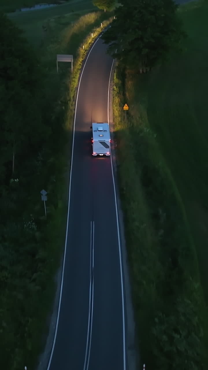 Vertical drone shot following a RV with lights on, driving on the countryside
