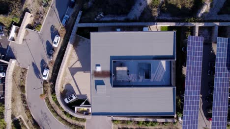 fotografía aérea de un edificio cuadrado con paneles solares alineados en el estacionamiento y coches estacionados debajo