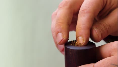 Cerca-De-La-Mano-De-Los-Hombres-Con-Dedos-Amarillentos-Y-Uñas-Muy-Cortas-Llenando-Una-Pipa-Con-Tabaco-Recién-Secado-En-Una-Pared-De-Fondo-Blanco-Al-Aire-Libre-Nublado-Incluso-Iluminación-Suave-Mal-Hábito-Riesgo-Para-La-Salud