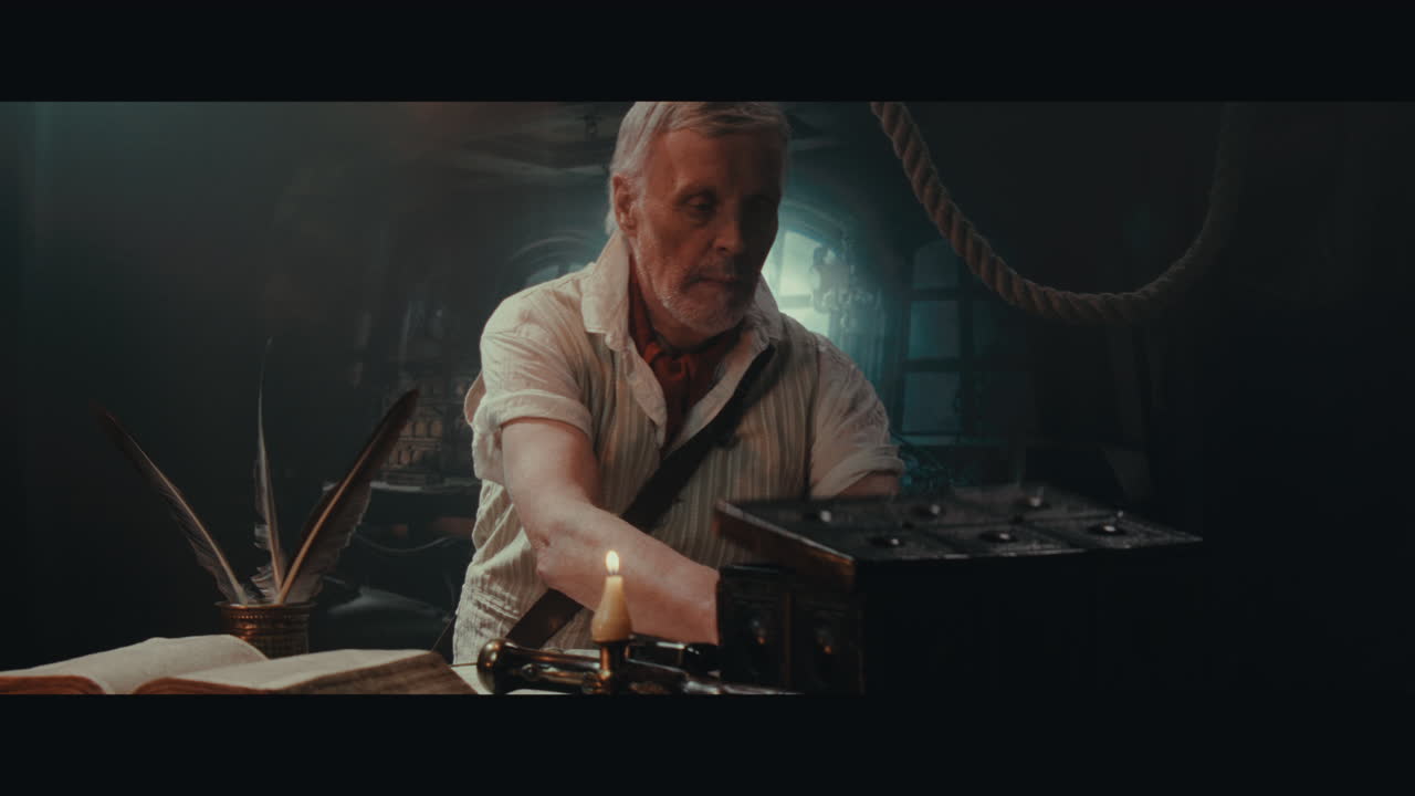 An old captain sits down by the old table inside the sailing ship cabin and writes a letter