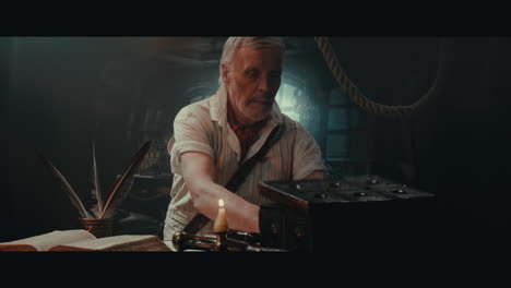 an old captain sits down by the old table inside the sailing ship cabin and writes a letter