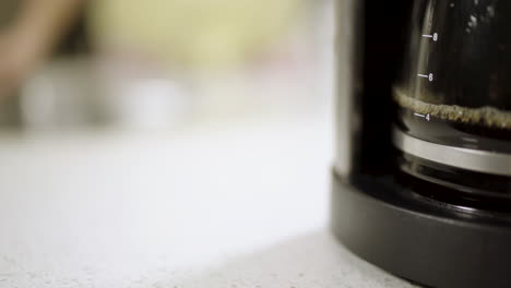 pan to coffee maker brewing from someone out of focus in the kitchen