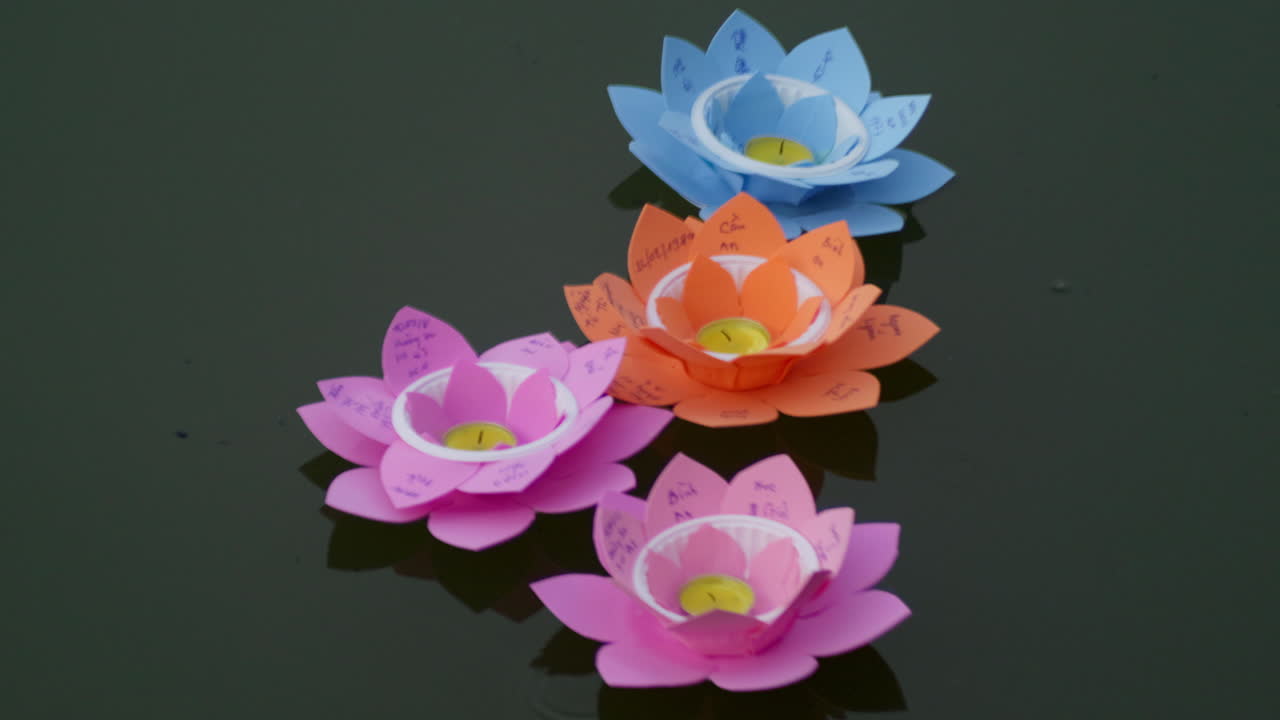 group of 4 paper light candle lotus flower shape floating on river water at night for annual Vesak Buddhist festivals celebration in south East Asia