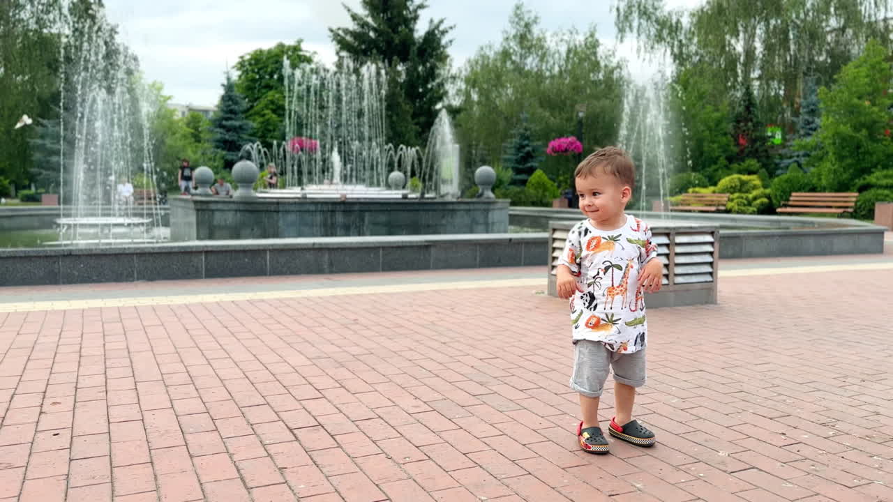 Adorable Caucasian baby boy running cheerfully by the square. Lovely toddler spending time outdoors in summer.