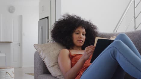mujer leyendo un libro mientras está acostada en el sofá en casa