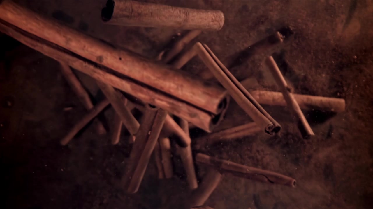 Kanelstenger som faller ned på et lag med kanelpulver i sakte film