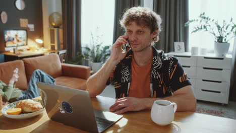 man using laptop and talking on phone as working remotely from home