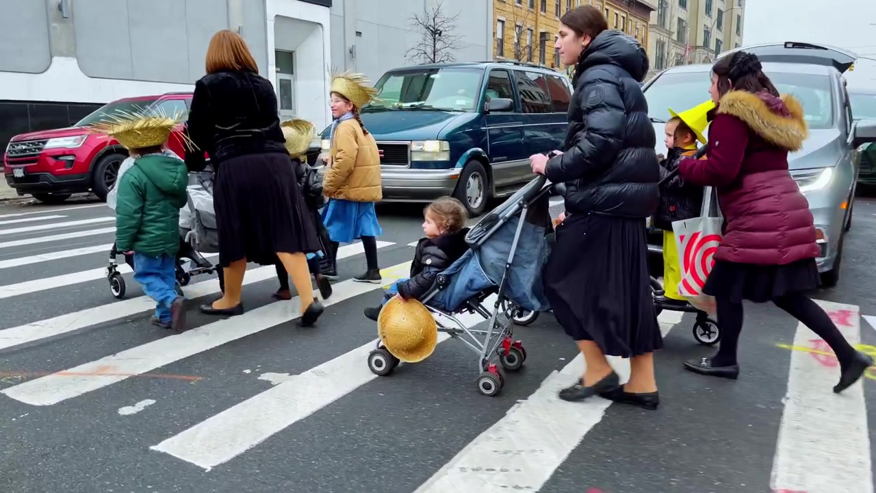 New York, USA, 9 marzo 2022: Primo piano delle ruote di un passeggino che attraversano un passaggio pedonale dipinto a New York. Primo piano dal basso delle ruote del passeggino, cappello di paglia e piedi di pedoni che attraversano le strisce pedonali dipinte.