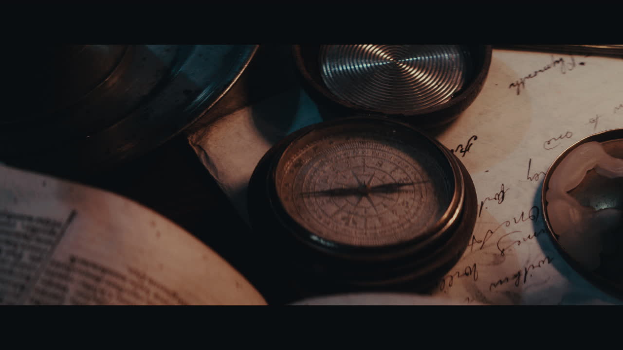 An old compass on the table filled with documents and maps inside the sailing ship cabin