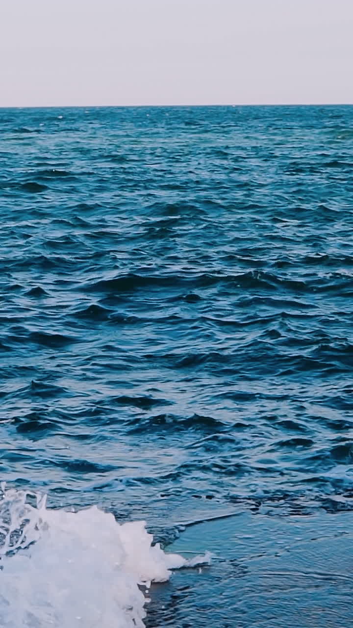 Waves crashing on stone beach. Amazing view of sea water. Blue water surface. Beautiful motion of sea water. Slow motion. Vertical video