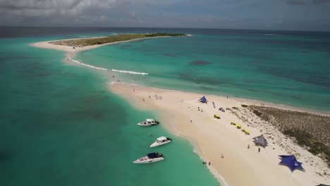 Archipiélago-De-Los-Roques-En-Venezuela-Con-Aguas-Cristalinas-De-Color-Turquesa,-Barcos-Y-Bañistas-Bajo-Coloridas-Sombrillas,-Vista-Aérea