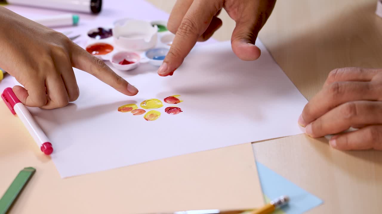 Adult and child create colorful fingerprint art on white paper using paint palette, natural lighting