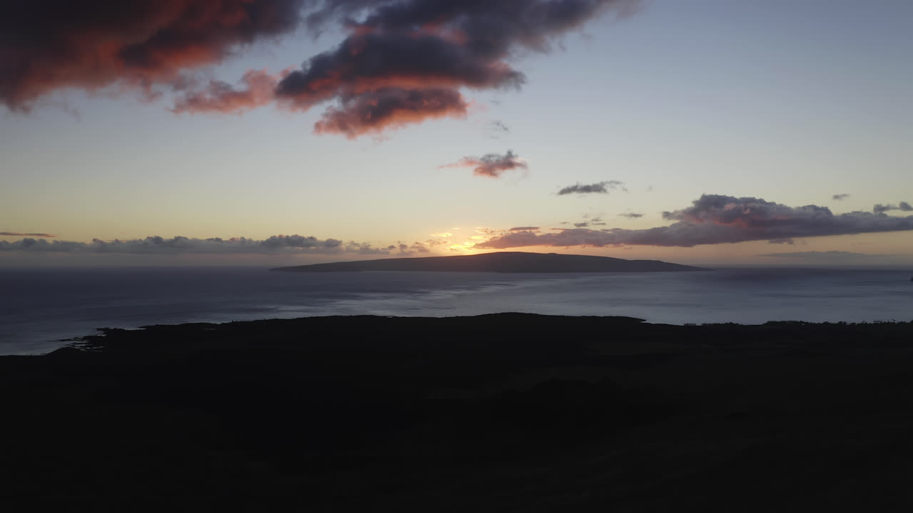 la última luz del sol se pone sobre kahoolawe mientras el resplandor rojo rodea las nubes y la silueta de maui.