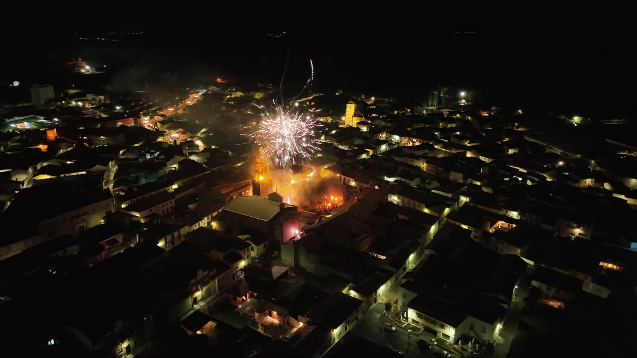 Smooth drone shot capturing fireworks lighting up the night sky over Mayorga, Spain, during El Vítor celebration, with rooftops and streets of the village illuminated below