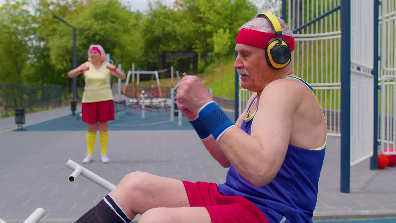 abuelo mayor con auriculares escuchando música desde el teléfono móvil en el patio de recreo y bailando