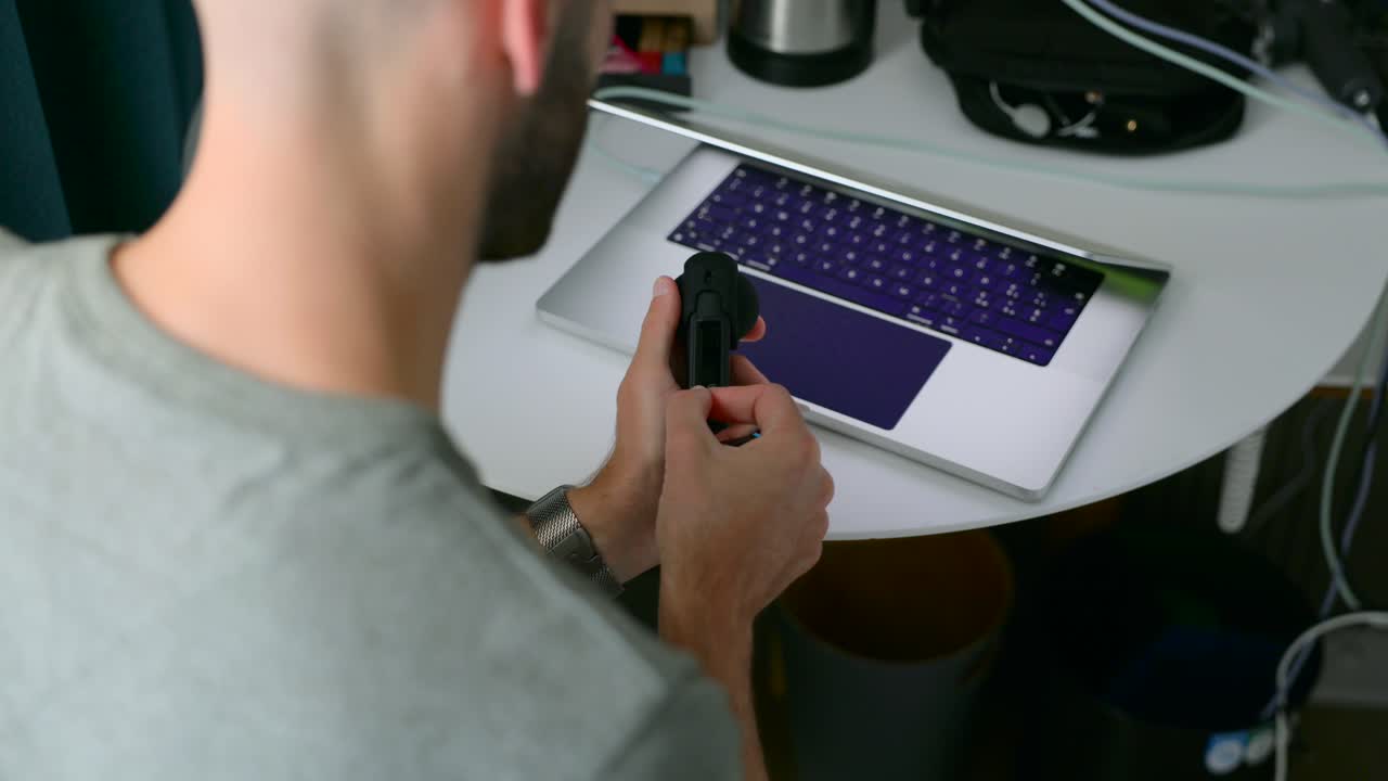 Inquadratura alle spalle di un uomo che inserisce una scheda SD in una fotocamera a 360 gradi Insta360 X4. È seduto a una scrivania con un laptop. Ideale per i concetti di workflow di vlogging e creazione di contenuti.