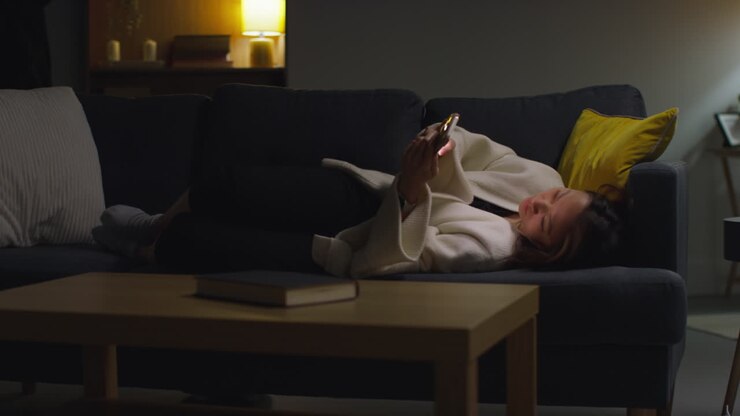 Woman Spending Evening At Home Lying On Sofa With Mobile Phone Scrolling Through Internet Or Social Media 18