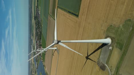 vertical video of rotating wind turbines along a river in a field on a sunny day