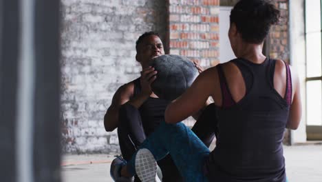 hombre y mujer afroamericanos haciendo ejercicio con una pelota de medicina en un edificio urbano vacío