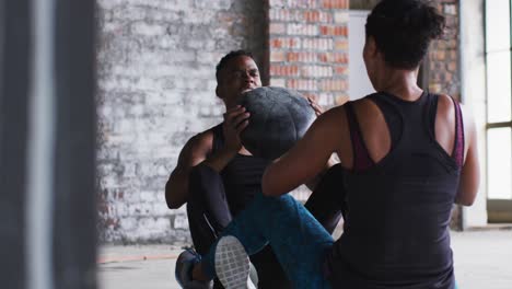 african american man and woman exercising with medicine ball in an empty urban building