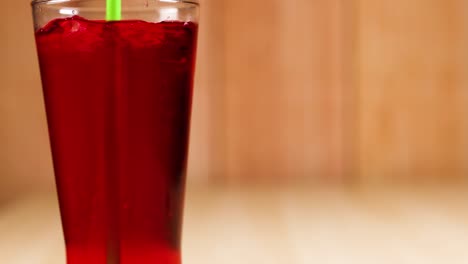 a green straw stirs a red beverage