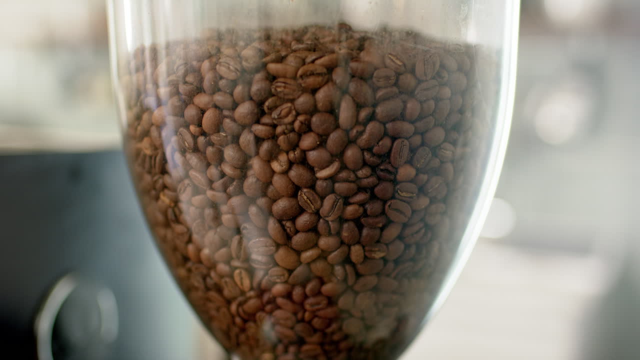 Um recipiente transparente está cheio de grãos de café marrons.