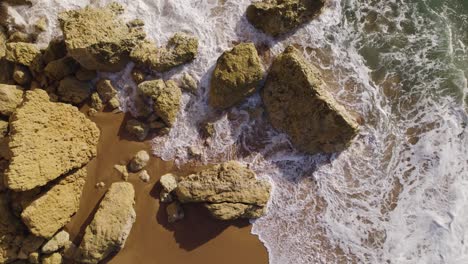 Waves-crashing-and-splashing-on-rocky-shore-creating-foam,-serene-coastal-beauty,-birds-eye-view