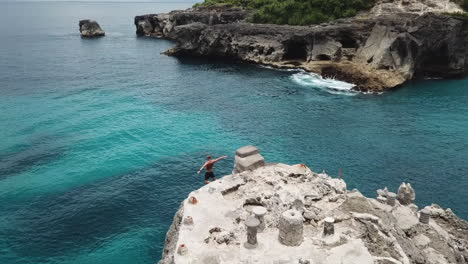 Aerial-follows-young-man-cliff-jumping-into-calm-tropical-sea-in-Bali