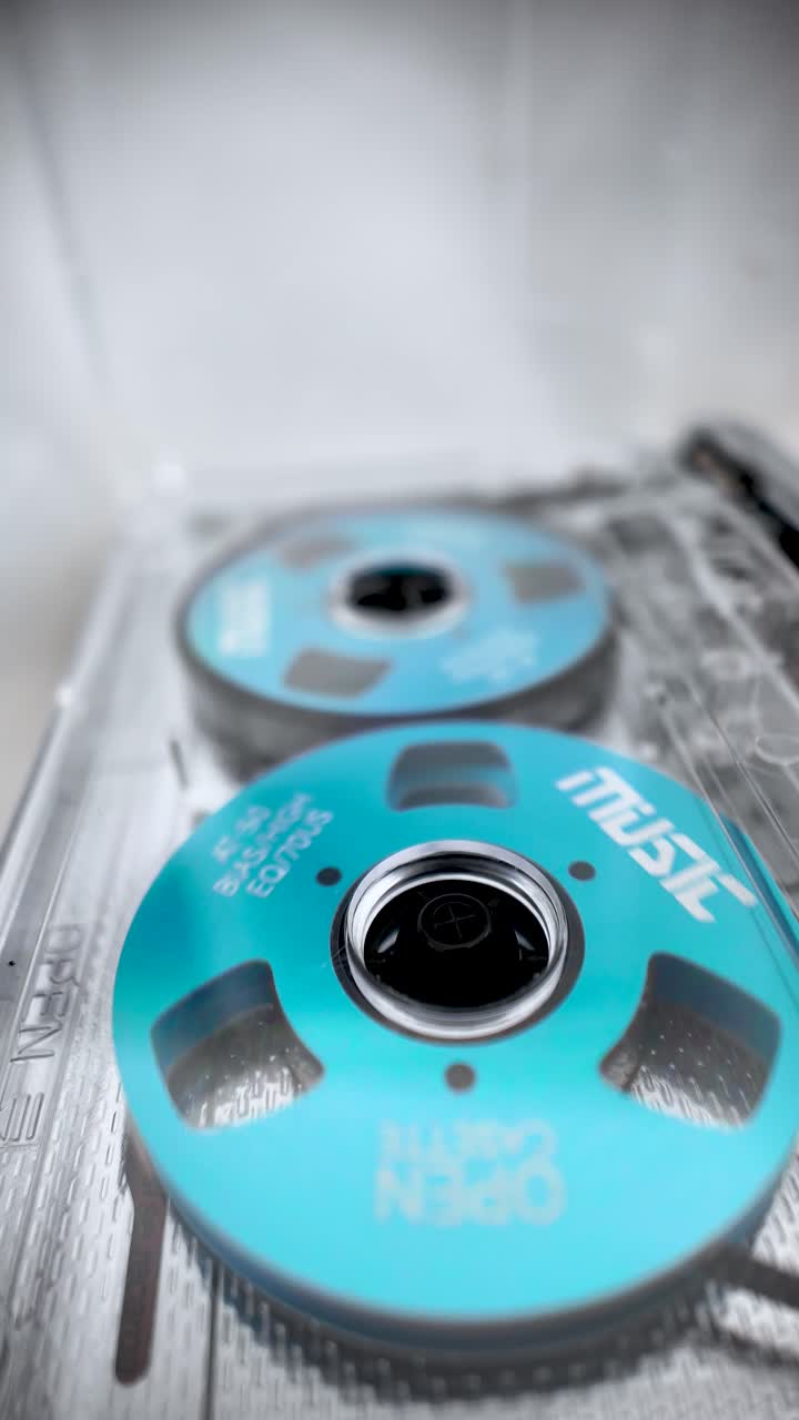 Gennemsigtig bærbar kassetteafspiller med synlige blå spoler, vintage musikkassetter og retro lydaestetik. Vertikal video.