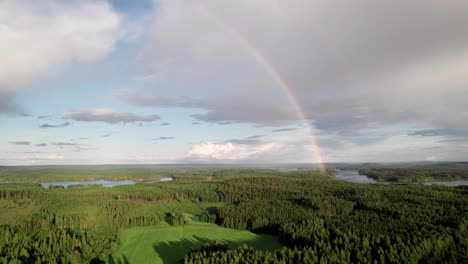 stunning rainbow over beautiful serene forest and lake landscape in finland, near kuopio, camera rising up