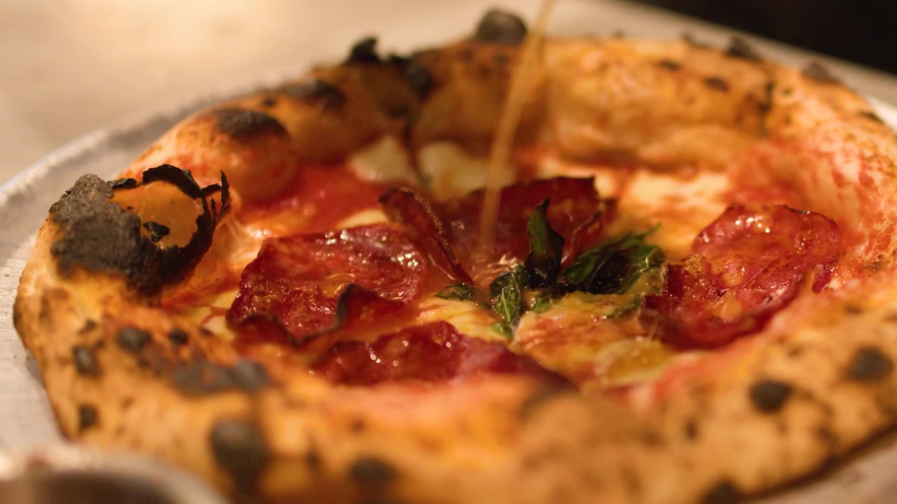 Primo piano di pizza artigianale con un filo d'olio d'oliva sulla crosta carbonizzata nella cucina di un ristorante.