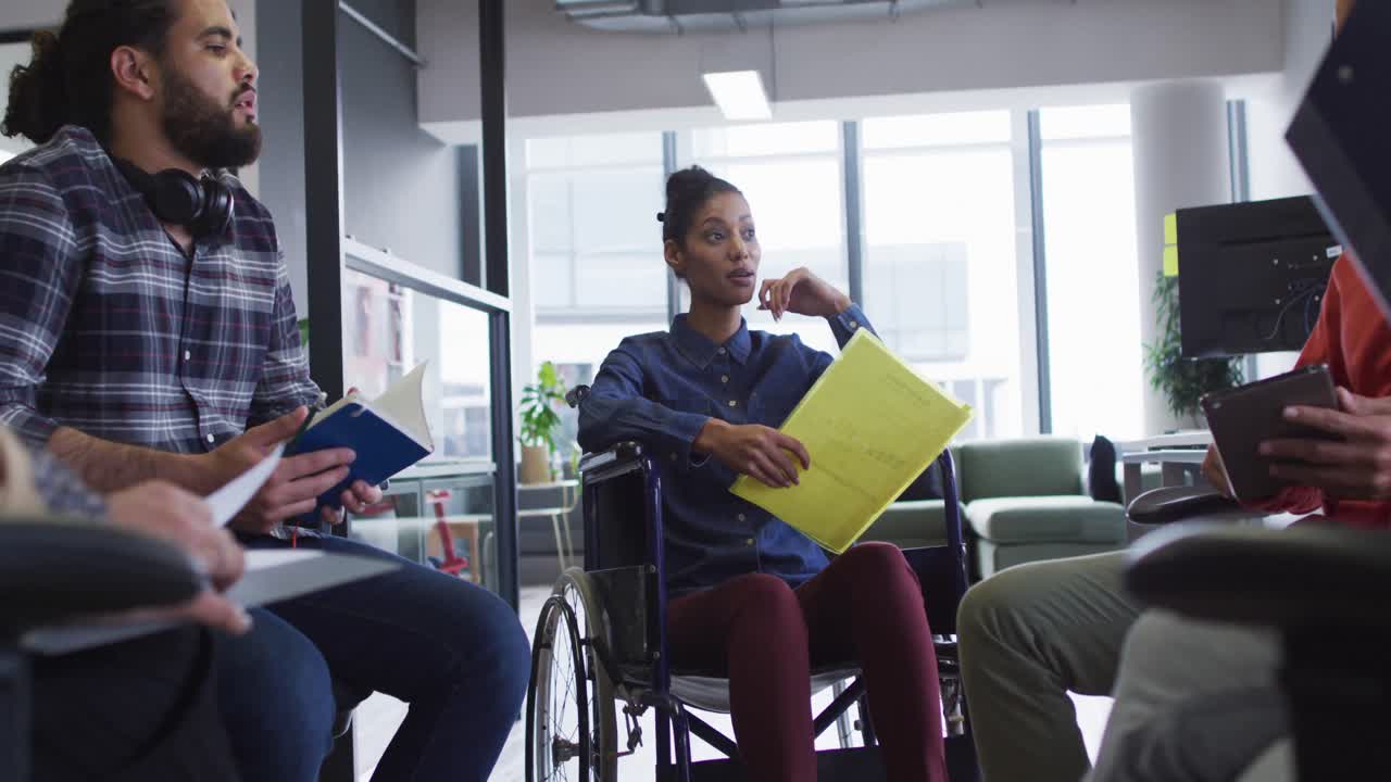 Mixed race businesswoman sitting in wheelchair discussing with diverse group of colleagues