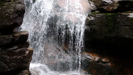 A-waterfall-runs-down-multiple-stone-ledges-and-feeds-into-a-calm-stream-within-a-gorge