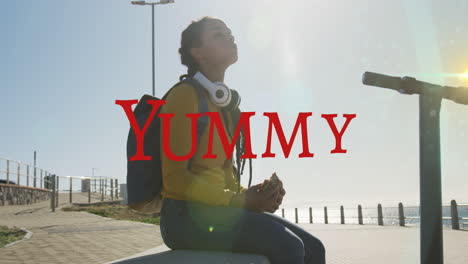 animation of yummy text over biracial woman with scooter eating on promenade