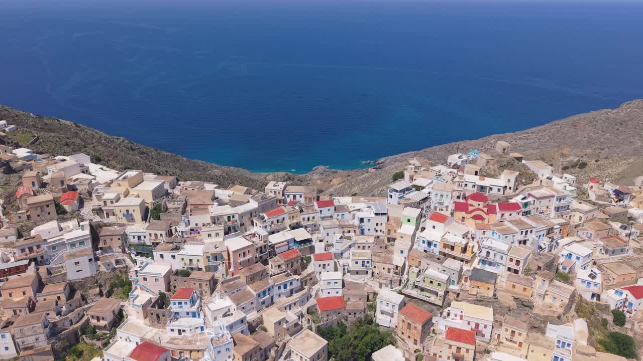 Drone pull-back and tilt-up movement reveals the colorful traditional village of Olympos in Karpathos, built on the hillside of the mountain with stunning Aegean scenery