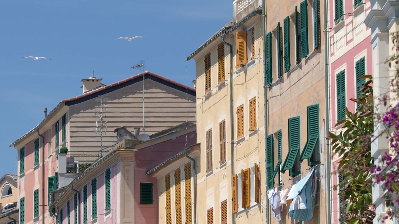 Inquadratura statica di vivace architettura della Riviera Italiana con bucato appeso alle finestre sotto la luce intensa del sole.
