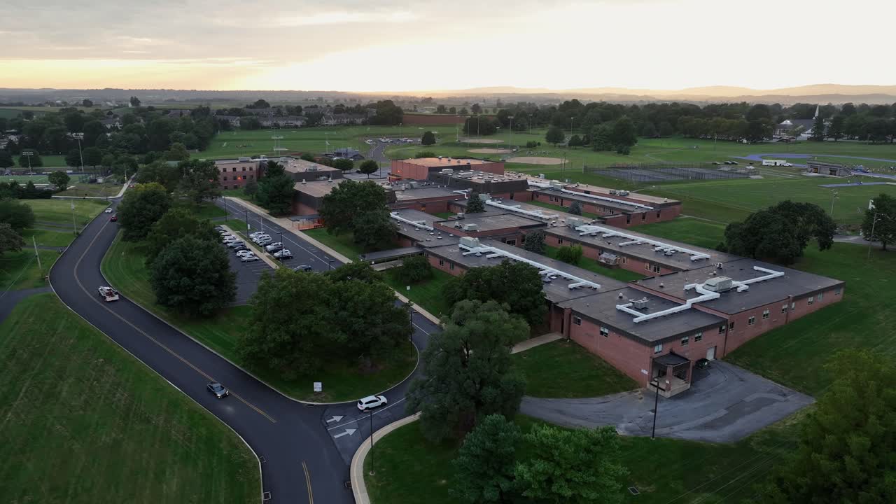 Driving cars arriving American high school at sunrise. Red brick buildings and large campus with sport area. Aerial wide shot. Ephrata, Pennsylvania