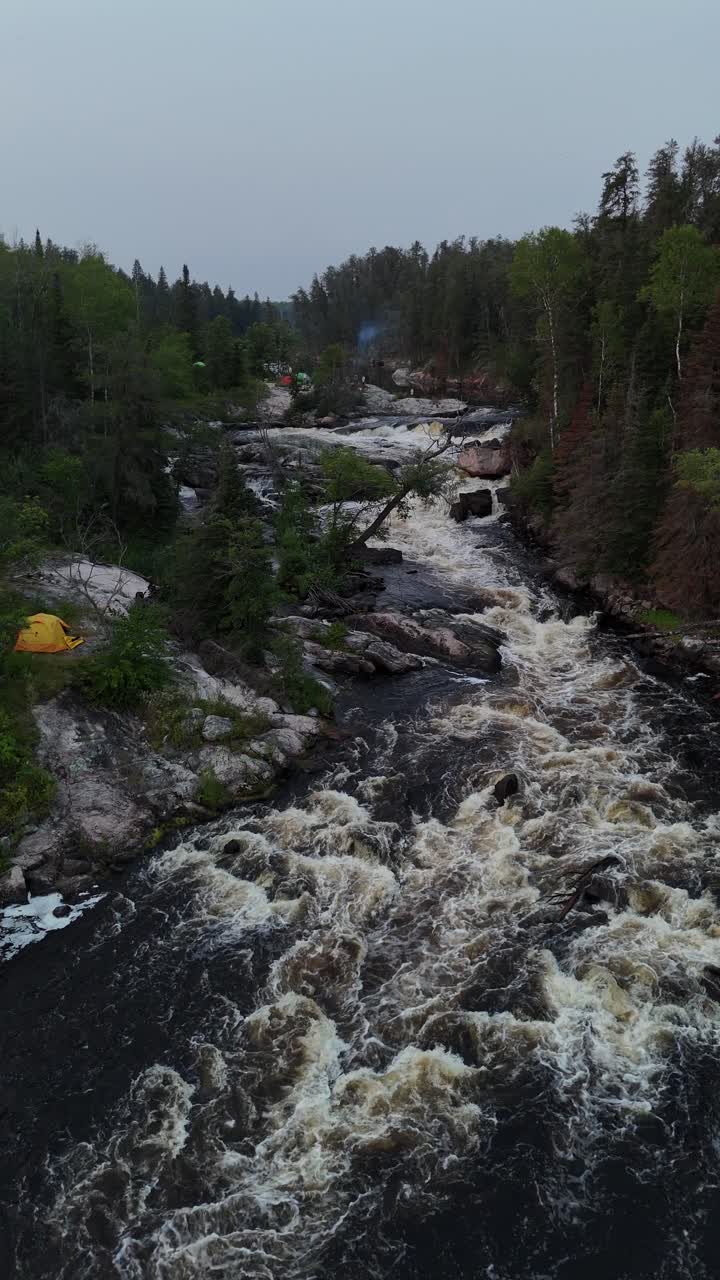 Turtle Falls på Manigotagan-floden i Manitoba, der strømmer over canadisk skjoldgranit. Et vertikalt luftfoto set nedstrøms viser hvide strømfald og et telt ved flodbredden i sommerens boreale skov