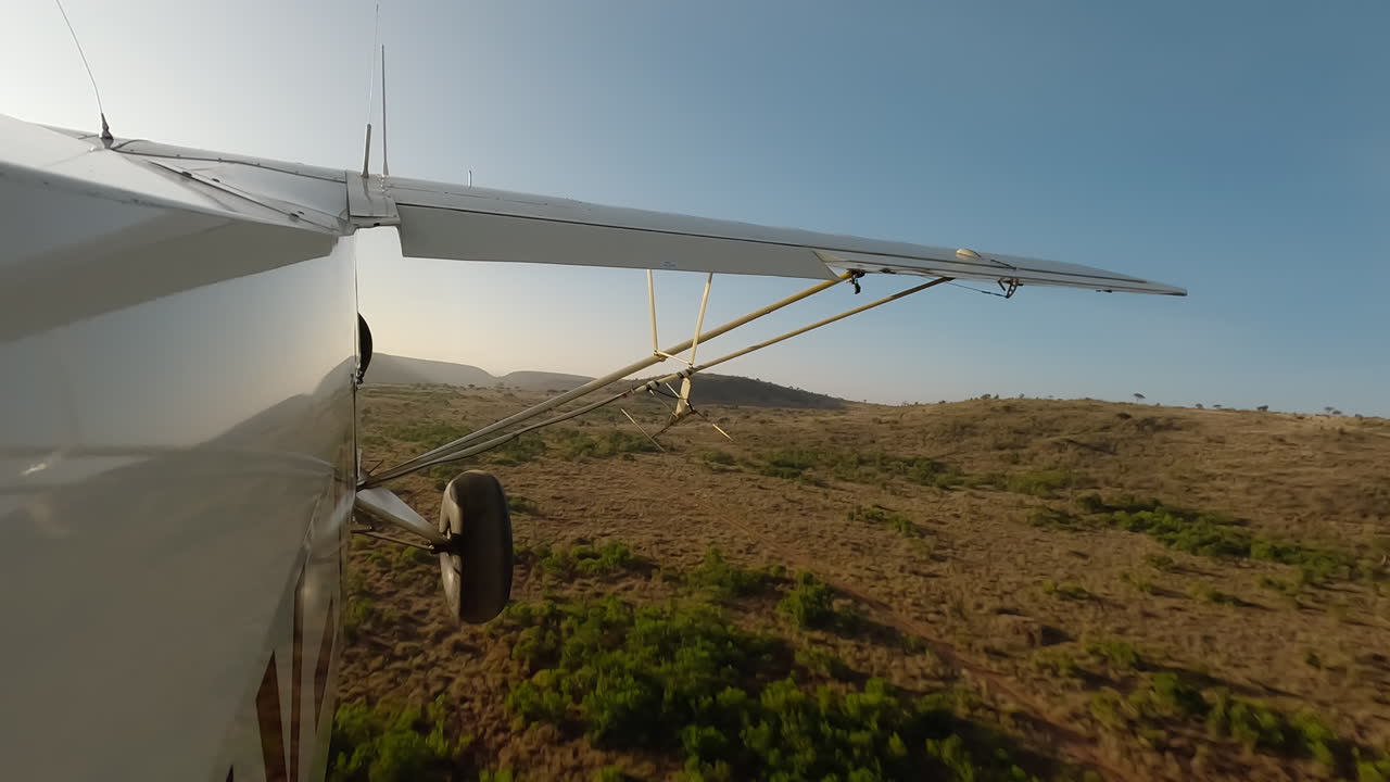 Kleines Flugzeug in Seitenansicht über trockenen Gräsern, Sträuchern und Hügeln