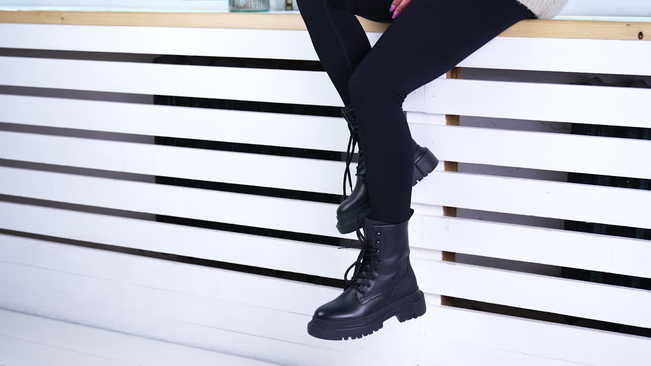 Female model sitting on the widow-sill demonstrating her footwear. Lady in black pants shows the black tractor boots with laces.