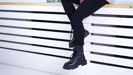 female model sitting on the widow-sill demonstrating her footwear. lady in black pants shows the black tractor boots with laces.