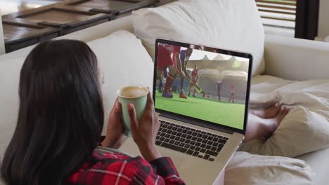 compuesto de una mujer sentada en casa sosteniendo un café viendo un partido de hockey en una computadora portátil