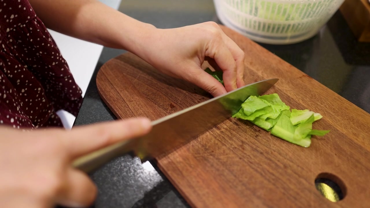 Close-up of a chef's hands slicing lettuce with a knife on a wooden board