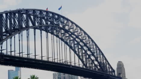 Turistas-Escalando-El-Puente-Del-Puerto-De-Sydney-Mientras-Las-Banderas-Aborígenes-Y-Australianas-Ondean-Sobre-Sus-Cabezas,-En-Australia